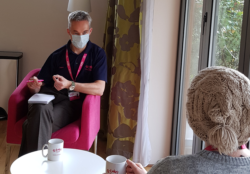 A photograph of our Chaplain Mark Newitt speaking with a patient. He is listening intently and wears a face mask.