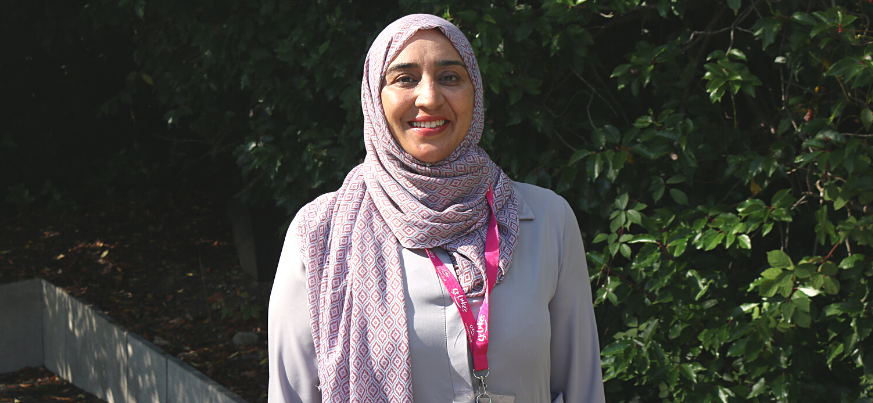 A portrait photo of Naureen Khan from Patient Services. She smiles to the camera and stands in the St Luke's gardens.